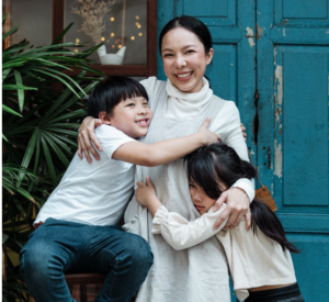 Happy Asian mother hugging her son and daughter, smiling with joy, representing a family qualifying for down payment assistance.