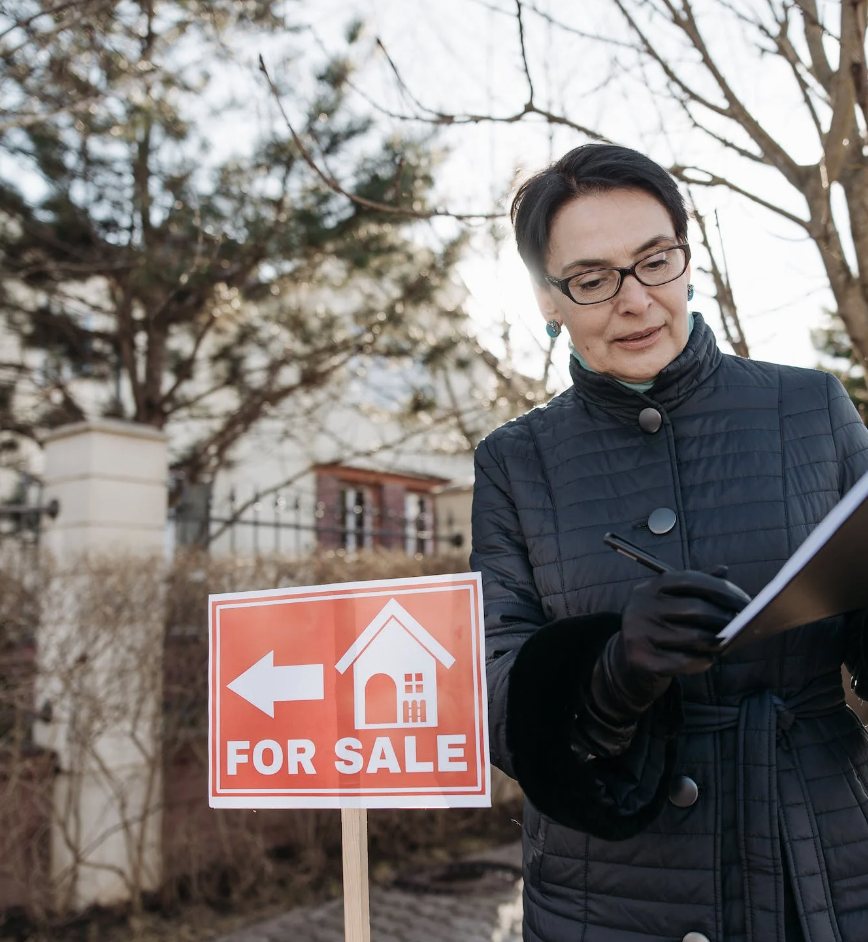 Real estate agent standing next to a 'House for Sale' sign, representing the differences between today's housing market and the 2008 crisis.